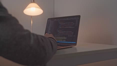 Young-male-hands-appear-and-move-toward-an-open-laptop-computer-where-software-editing-code-is-on-display