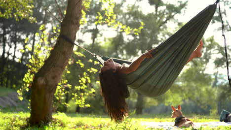 Beautiful-mixed-race-woman-with-long-black-hair-relaxing-in-hammock-while-camping-with-his-dog-in-wilderness-during-a-sunny-day-of-summer