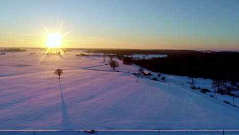 A-sunny,-snowy-landscape-during-a-golden-sunrise-and-long-shadows-from-the-countryside-trees---sliding-aerial-flyover