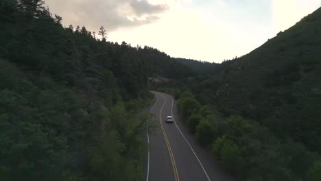 Tracking-Aerial-View-of-White-Car-Moving-on-Empty-Road-in-American-Countryside-at-Twilight,-Drone-Shot