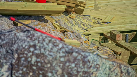 Static-shot-of-a-worker-constructing-wooden-pier-on-a-rocky-shore-in-timelapse