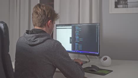 A-young-man-sits-down-at-his-home-office-desk-and-immediately-starts-editing-source-code-on-his-computer-to-further-his-career-in-software-development