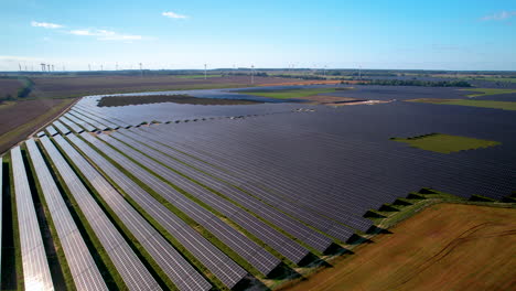 Aerial-flyover-modern-solar-farm-and-wind-turbine-park-in-background-on-summer-day