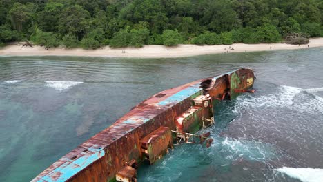 Rusty-Shipwreck-Laying-on-its-Side-as-Waves-Crash-in-Pangandaran,-Indonesia