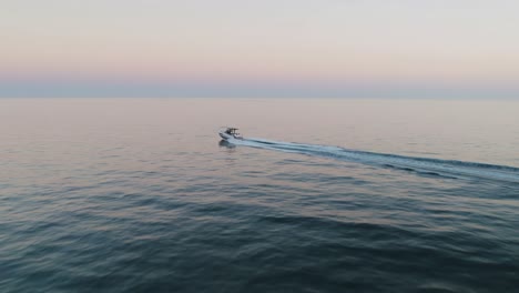 Aerial-of-speedboat-passing-by-near-the-coastline-of-Marbella,-Spain,-during-sunset