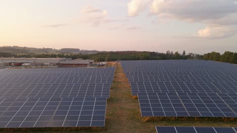 Slow-Aerial-Dolly-Down-The-Middle-Gap-Of-A-Solar-Panel-Field-With-The-Sun-Setting-In-The-Background-Hesse,-Germany