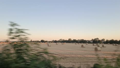 View-From-A-Moving-Irish-Rail-Train-Passing-Through-The-Countryside-Field-With-Rolls-Of-Round-Hay-Bales-In-Ireland