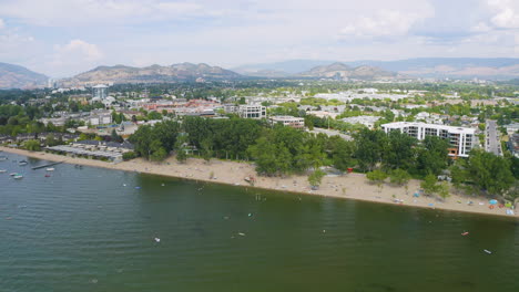 Establishing-aerial-view-of-Kelowna-BC-beach-with-the-community-and-mountains-visible-in-the-background