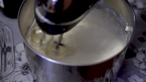 Top-shot-of-mixing-whipped-egg-whites-cream-in-steel-bowl-with-mixer-on-a-wooden-table
