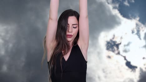 Long-hair-beautiful-caucasian-brunette-woman-wearing-boxing-wraps-stretches-arms-and-punches-toward-camera-with-clouds-moving-in-background