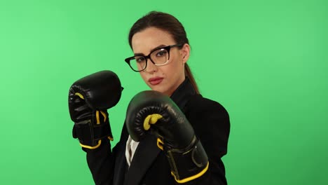 Businesswoman-with-glasses-and-ponytail-wearing-white-shirt-and-black-business-attire-uses-boxing-gloves-to-punch-toward-camera