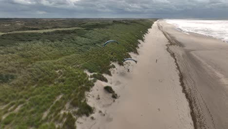 Spectacular-aerial-tracking-shot-of-active-Paraglider-soaring-over-sandy-beach-along-coastline-of-Sea