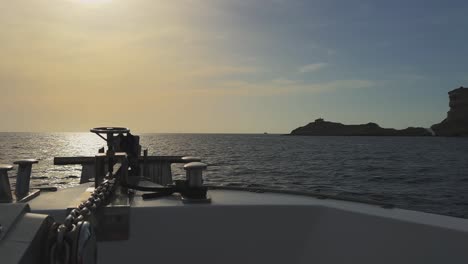 Perspektive-Vom-Segelbootbug-Mit-Strahlender-Sonne-Im-Vordergrund-Und-Felsen-Der-Insel-Korsika-Und-Leuchtturm-Capo-Pertusato-Im-Hintergrund,-Frankreich