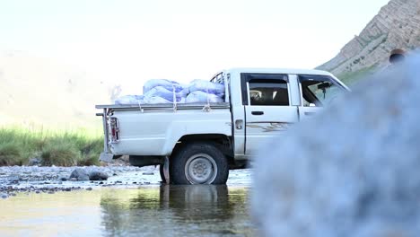 Close-up-shot-the-jeep-carrying-numerous-sacks-of-grains-and-other-necessaries-and-supplies-is-stopped-at-stream-of-the-river