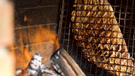 Lamb-rib-in-grid-on-side-of-wood-fire-dripping-with-fat-as-it's-being-barbecued