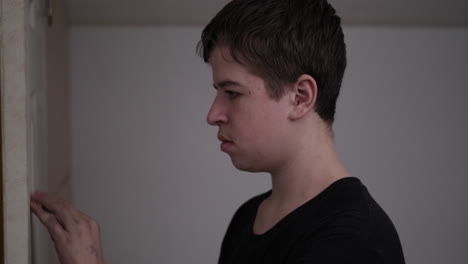 A-young-high-school-aged-teen-boy-looking-angry,-troubled,-depressed-and-sad-closes-the-door-to-his-bedroom