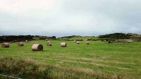 Countryside-pasture-with-rolled-straw-hay-bale-in-open-overcast-British-farmland