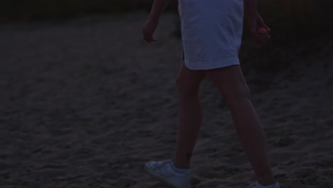 Tilt-up-of-young-woman-walking-trough-sand-dunes-at-dusk