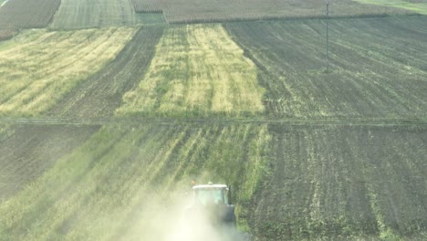 Drone-shot-behind-working-tractor-plowing-green-agricultural-field-during-sunlight---Animals-following-vehicle