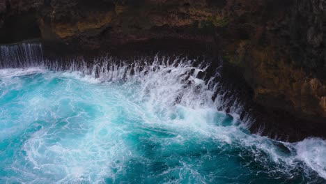Static-aerial-shot-of-intense-blue-waves-crashing-against-the-rocks-of-cliff