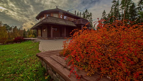Timelapse-shot-of-dried-red-leaves-on-a-warm-autumn-day-in-rural-countryside-with-view-of-beautiful-cottage-in-the-background