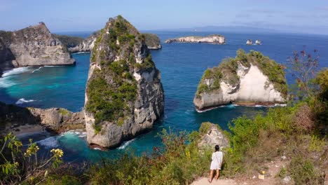 Young-woman-walking-towards-edge-of-coastal-cliff-overlooking-the-tropical-rock-islands-of-Nusa-Penida