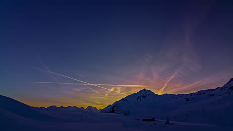 Time-lapse-shot-of-colorful-sky-after-sunset-behind-snowy-mountains-and-clear-blue-sky-with-flying-airplanes
