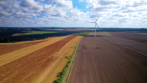 Aerial-dolly-slide-across-colourful-agricultural-farmland-with-wind-turbine-rotating-slowly-in-the-breeze
