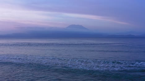 Aerial-view-of-waves-coming-towards-camera-and-Agung-volcano-in-background-at-sunset