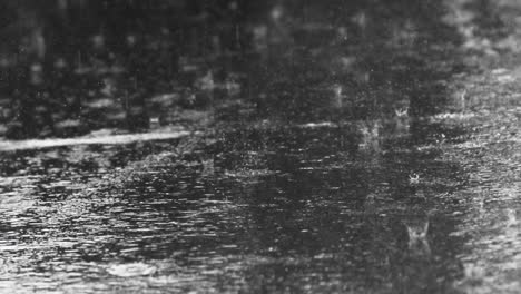 Close-up-shot-of-heavy-raindrops-shattering-on-an-asphalt-road-in-the-rain