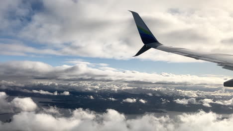 Airplane-wing-tip-turning-and-descending-above-the-clouds