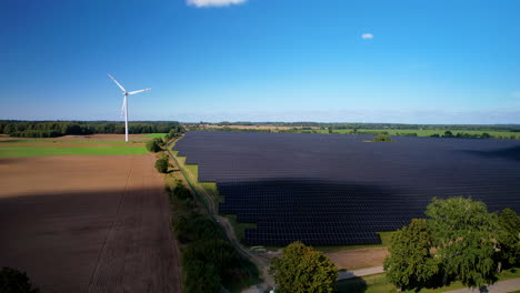 Rising-aerial-view-cloud-shadows-passing-across-solar-panel-array-and-wind-turbine-on-agricultural-farmland