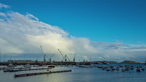 Time-lapse-of-boats-sailing-industrial-shipping-port-at-day-time-while-rainbow-appears-in-clouds
