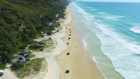 4K-Aerial-Drone-Over-4WD-Cars-Driving-On-Sandy-Beach-With-Blue-Ocean-Waves-Lapping-Shore-In-Australia