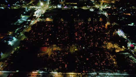 Aerial-view-overlooking-illuminated-graveyard,-during-Day-of-the-dead,-moody-evening-in-Mexico-city---pull-back,-drone-shot