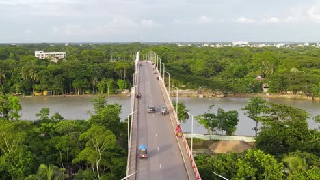 Absteigende-Luftaufnahme-Der-Viaduktbrücke-über-Den-Fluss-Mit-Bewaldetem-Flussufer,-Vorbeifahrende-Fahrzeuge,-Bangladesch