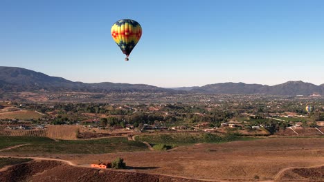 Colorful-Hot-Air-Balloon-Flying-Above-Sunny-Valley-and-Small-Town-in-Countryside-of-California-USA,-Aerial-View