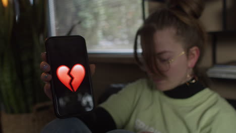 Chica-Con-El-Corazón-Roto-Mostrando-Su-Teléfono-Con-Un-Emoji-De-Corazón-Roto,-De-Mano,-Cerca
