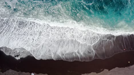 Crystal-clear-turquoise-ocean-waves-washing-black-sand-beach,-overhead