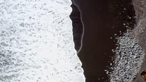 Foamy-waves-washing-black-sand-beach-of-Azores,-vertical-overhead-view