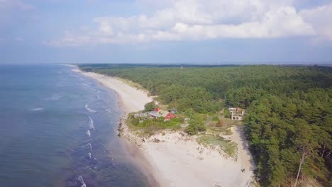 Aerial-view-of-Baltic-sea-coast-on-a-sunny-day,-white-sand-seashore-dunes-damaged-by-waves,-pine-tree-forest,-coastal-erosion,-climate-changes,-Cumulus-clouds,-wide-angle-drone-shot-moving-backward