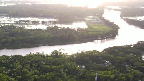 Aerial-view-of-harsh-light-reflection-on-overflowed-flooded-river,-Cultivation-fields-and-tropical-forest-flooded,-Catastrophe