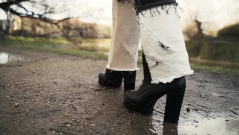 Young-woman-in-a-black-coat-walking-across-a-puddle-in-a-park-in-autumn-in-afternoon