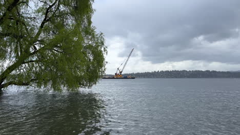 Ein-Kran,-Der-Schiffscontainer-Von-Einem-Lastkahn-An-Einem-Hafendock-Be--Und-Entlädt,-Wie-Von-Der-Olympic-Peninsula-In-Washington-Aus-Gesehen