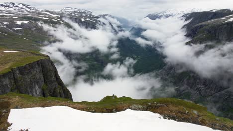 Drone-circling-around-a-hiker-standing-at-the-edge-of-steep-cliff-overlooking-the-clouds-forming-in-Simadalen-valley