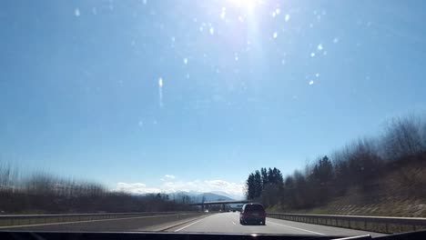 Driving-Timelapse-on-a-highway-with-tunnels-passing-other-cars-driving-on-a-sunny-day-with-a-blue-sky,-grassy-fields-with-trees-and-snow-covered-mountains-in-the-distance