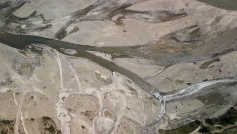 Aerial-top-down-view-above-dry-riverbank,-dirty-road-with-white-RV-Vehicle