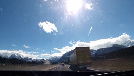 Driving-Timelapse-on-a-highway-passing-other-cars-driving-on-a-sunny-day-with-clear-blue-sky,-grassy-fields-with-trees-and-snow-covered-mountains-in-the-distance