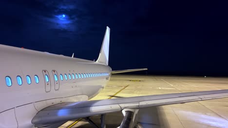 Ungewöhnliche-Und-Schöne-Nachtansicht-Des-Geparkten-Flugzeugs-Auf-Dem-Vorfeld-Des-Flughafens-Mit-Weißem-Körper,-Der-Rumpfflügelmotor-Und-Heck-Mit-Mond-Im-Hintergrund-Zeigt