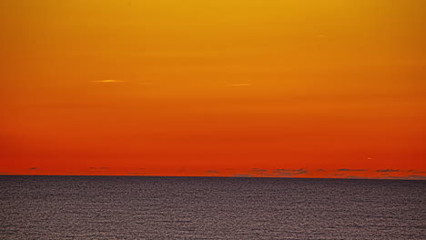 Zeitrafferansicht-Des-Meeres,-Das-Im-Orangefarbenen-Schein-Der-Untergehenden-Sonne-Am-Horizont-Verschwindet